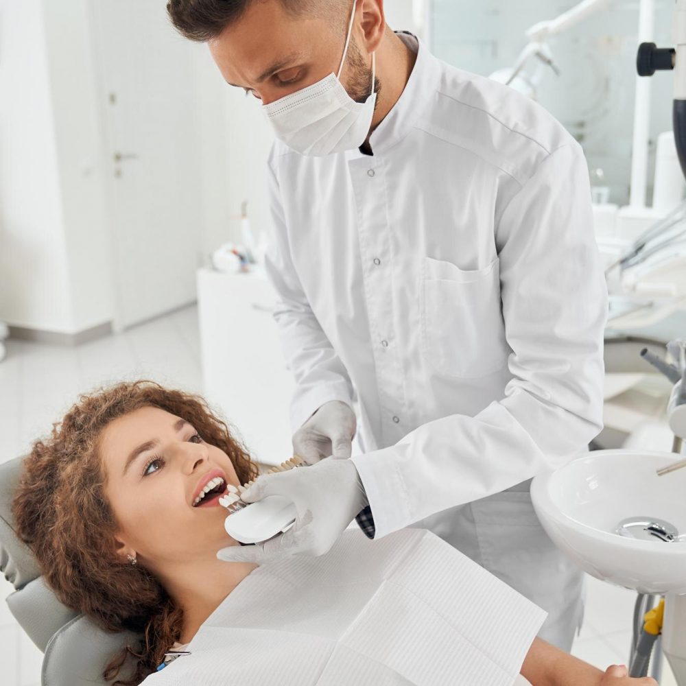 mulher-sorrindo-enquanto-dentista-masculino-mantendo-a-gama-de-cores-dos-dentes_651396-1399